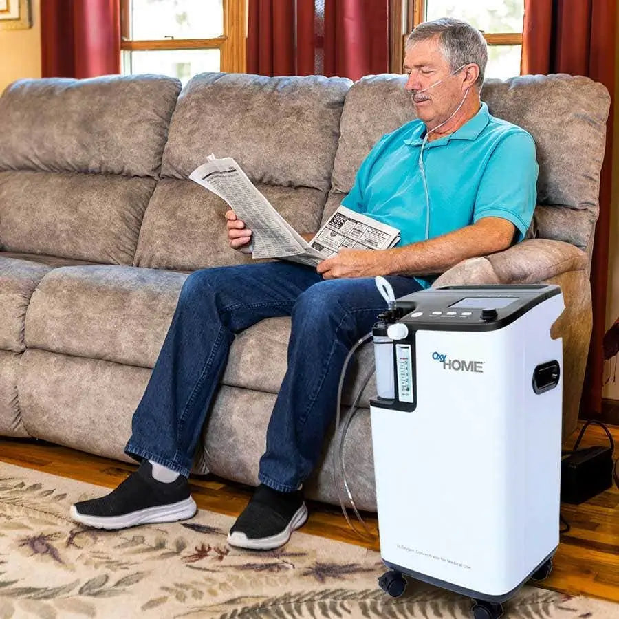 Man sitting on a couch reading a newspaper with an oxygen concentrator next to him.