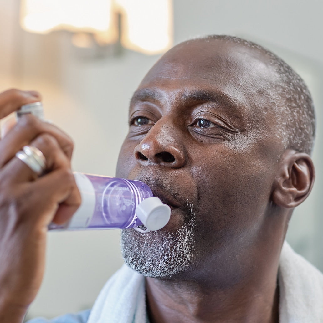 Man using a purple inhaler device with a blurred background