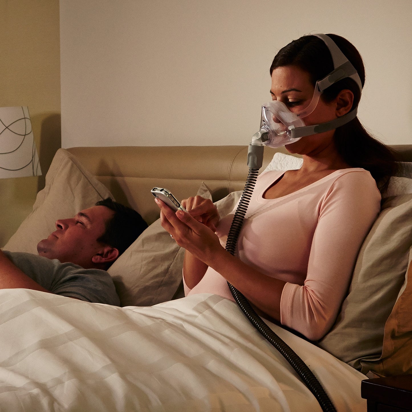 Woman using a CPAP machine while lying in bed with a man.