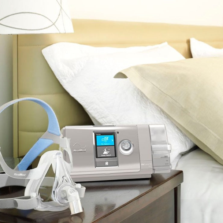 CPAP machine and mask on a nightstand next to a bed with pillows