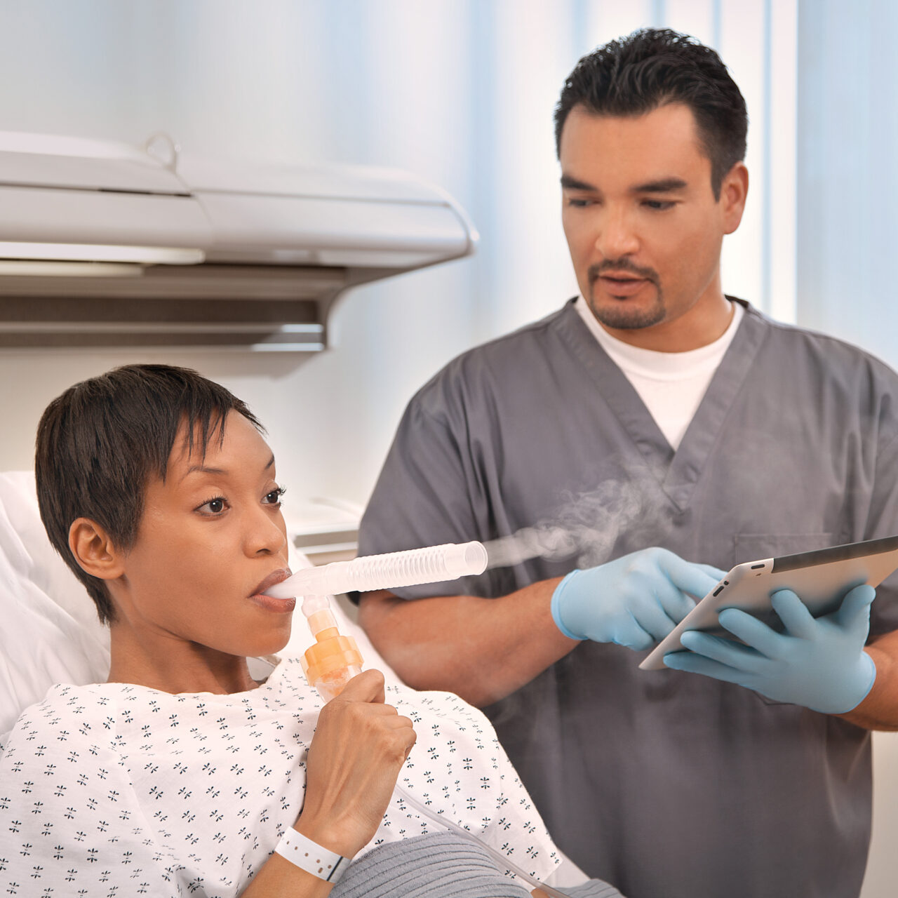 Doctor using a tablet with a patient in a hospital bed using a nebulizer