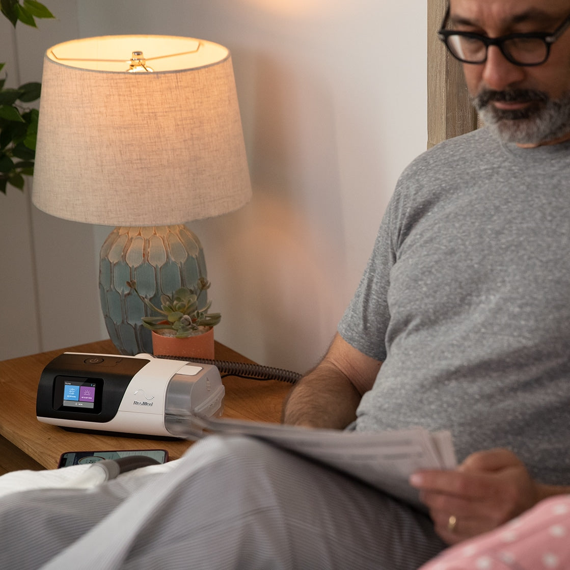 AirSense 11 CPAP Next to Man Reading in Bed