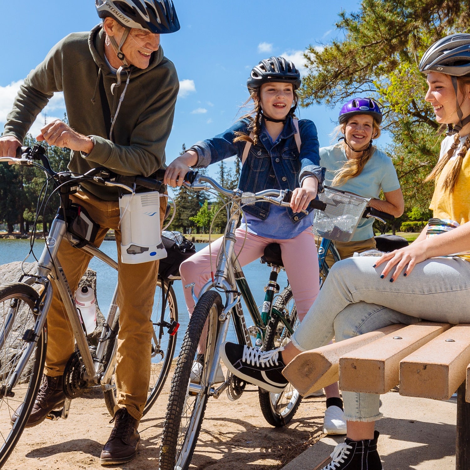 Family with bicycles by a lake on a sunny day with a man using a Caire Freestyle concentrator 