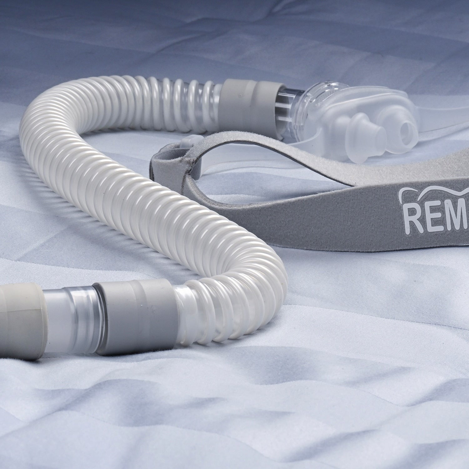 CPAP hose and mask on a textured surface with 'REM' branding.
