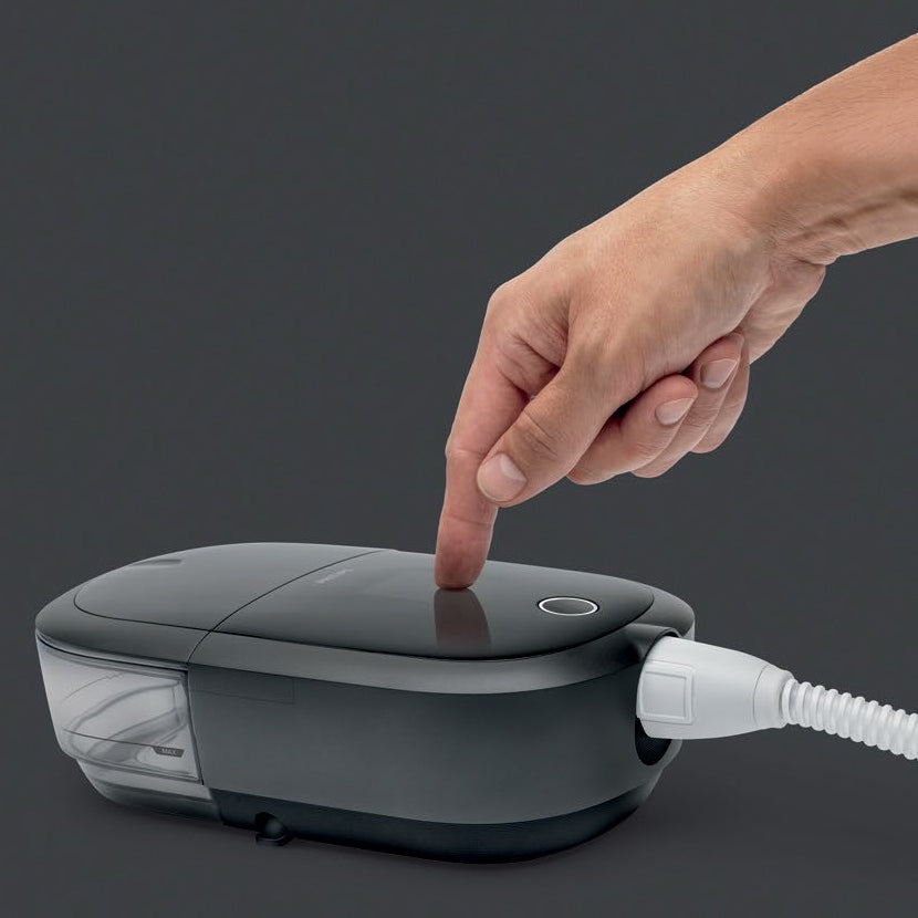 Hand pressing a button on a CPAP with a white hose against a dark background