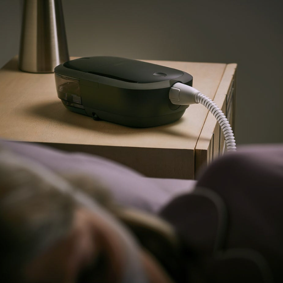 CPAP Machine with a white tubing on a wooden surface, with a blurred person in the foreground.