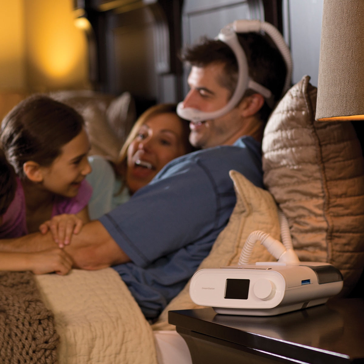 man and family with dreamstation auto cpap machine laughing in bed