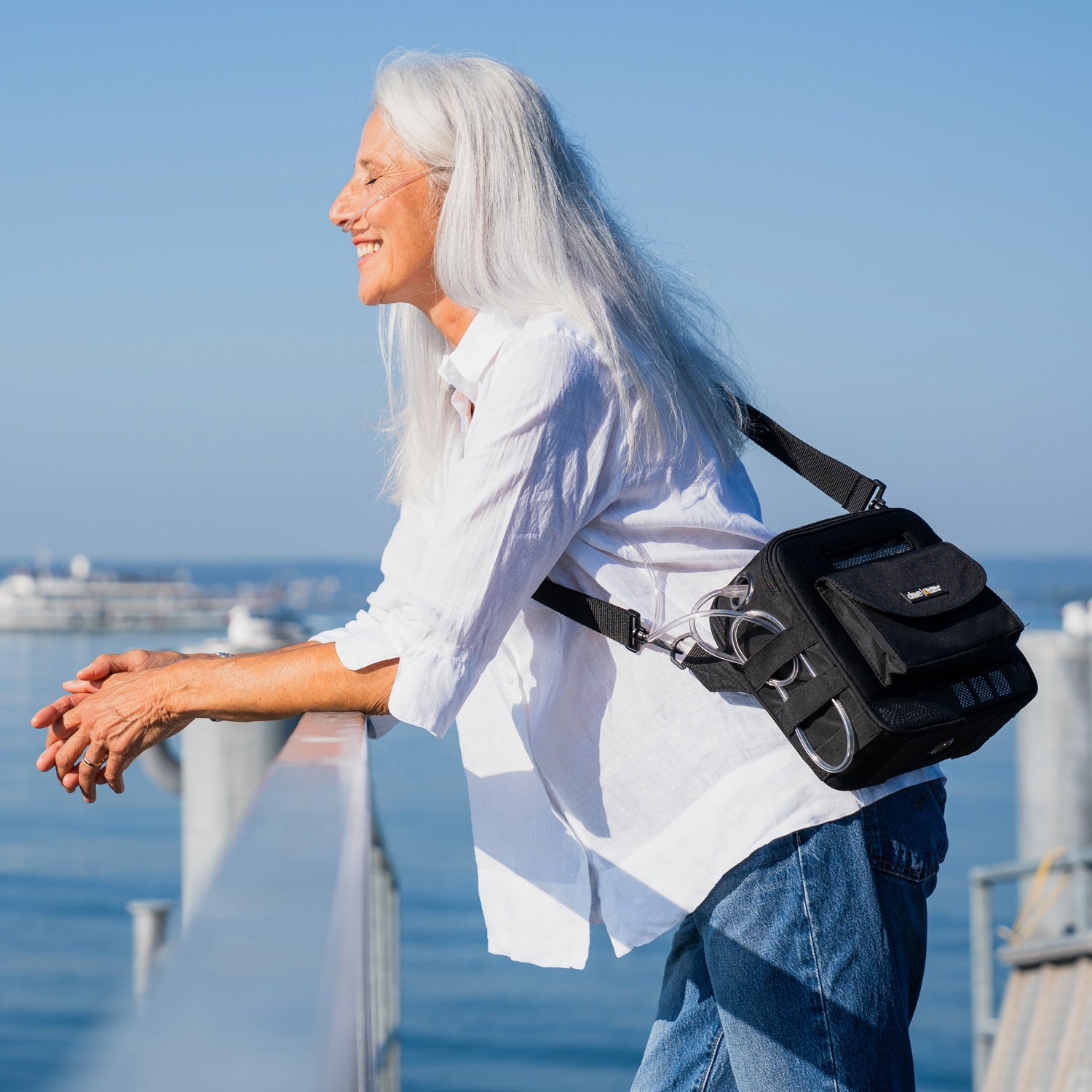 Woman with an iGo2 POC in a black bag standing by a waterfront with a clear blue sky.