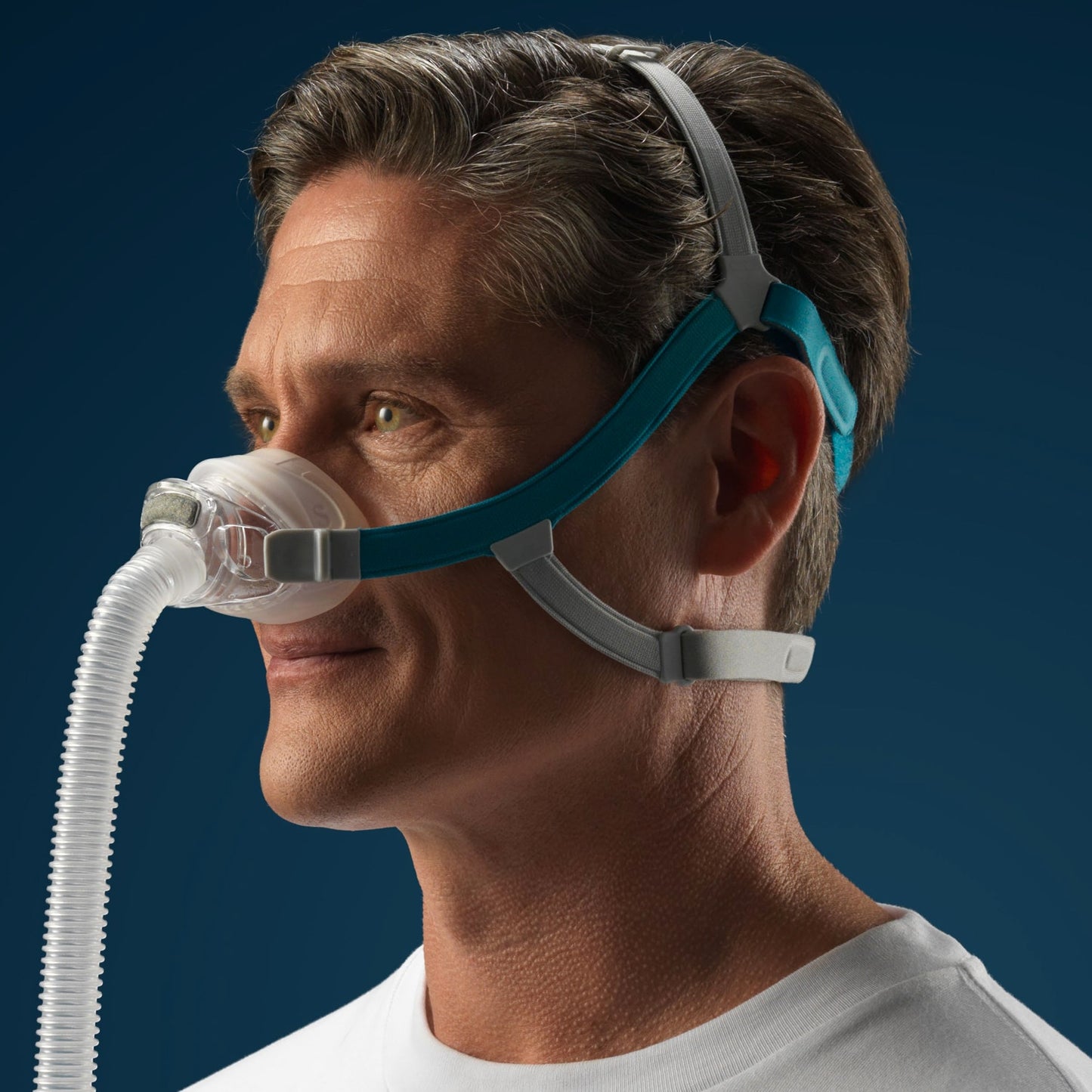 Man wearing a CPAP mask with a blue headgear against a dark background