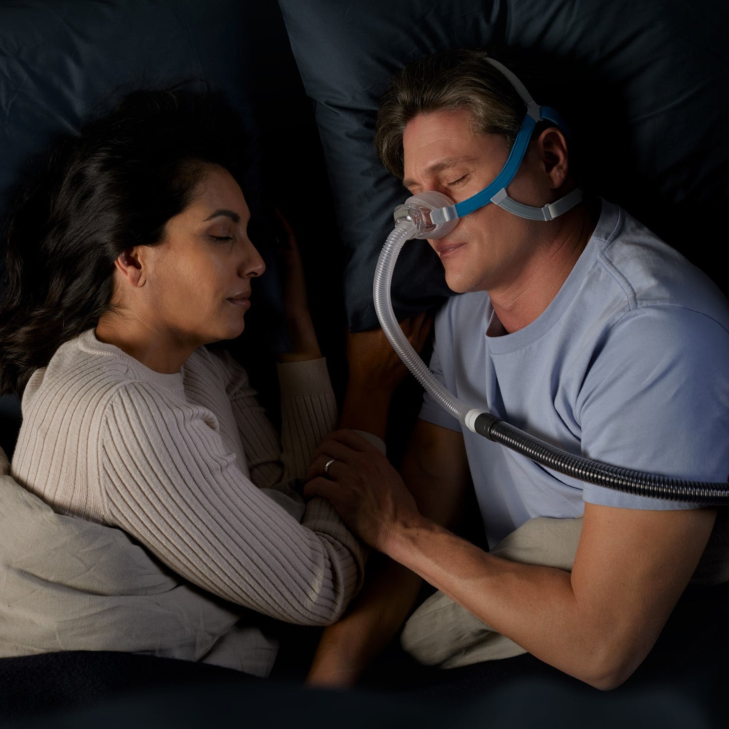 Man wearing a CPAP mask lying next to a woman in a dark room
