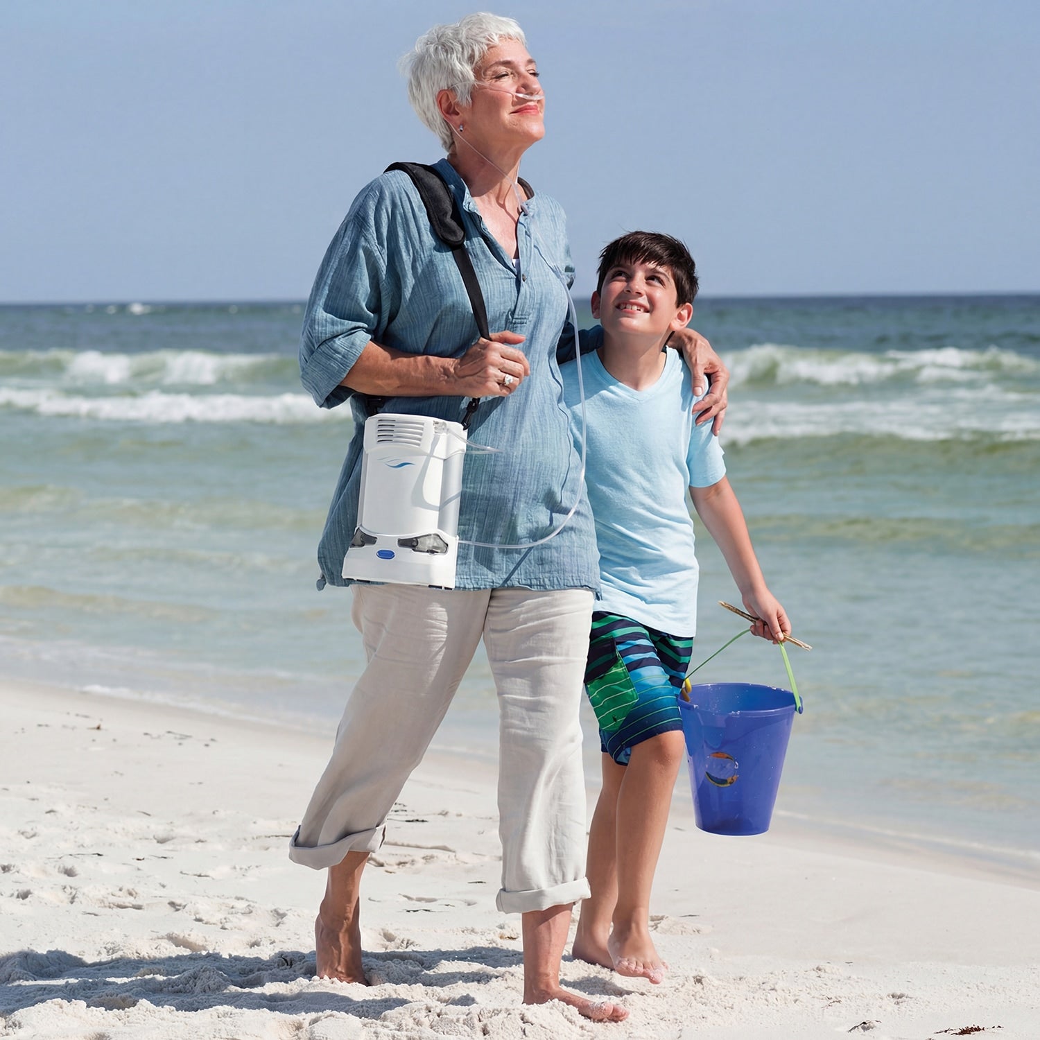 Woman wearing a Freestyle Portable concentrator walking on the beach with a child 