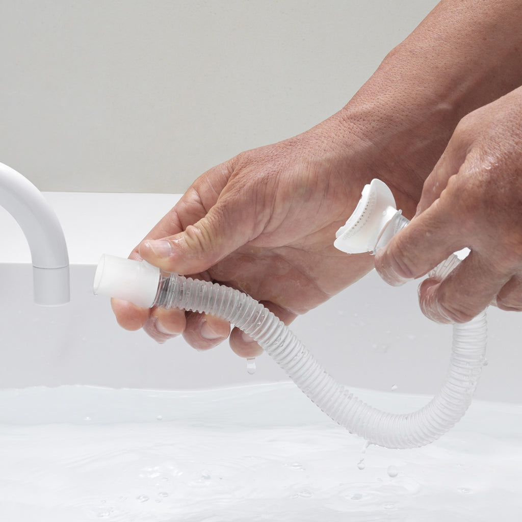 Person holding a white and clear hose with a white fitting against a light gray background