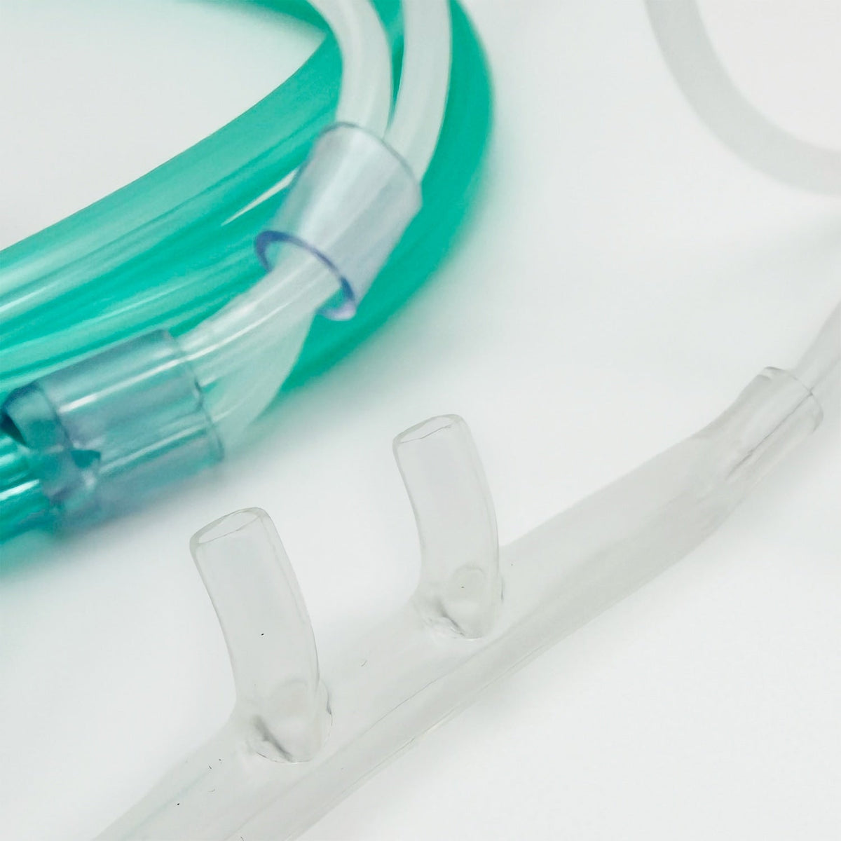 Close up of clear plastic nasal cannula tubes and a translucent green tube connector on a white background