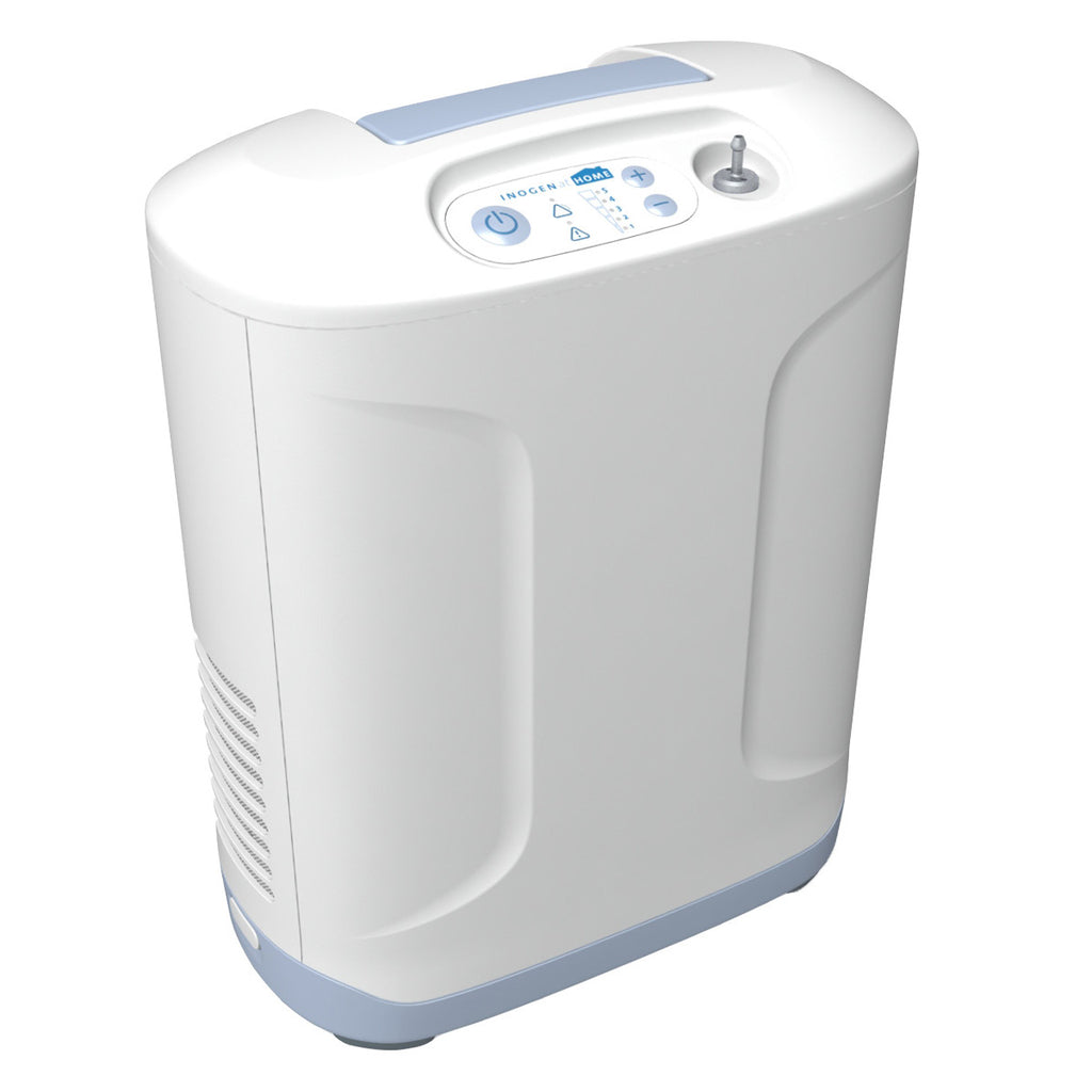A white Inogen At Home stationary oxygen concentrator with blue accents, featuring a digital display and control buttons on the front panel.