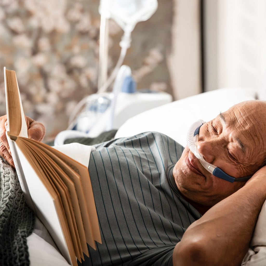 Man in bed reading and wearing myAIRVO blue cannula 