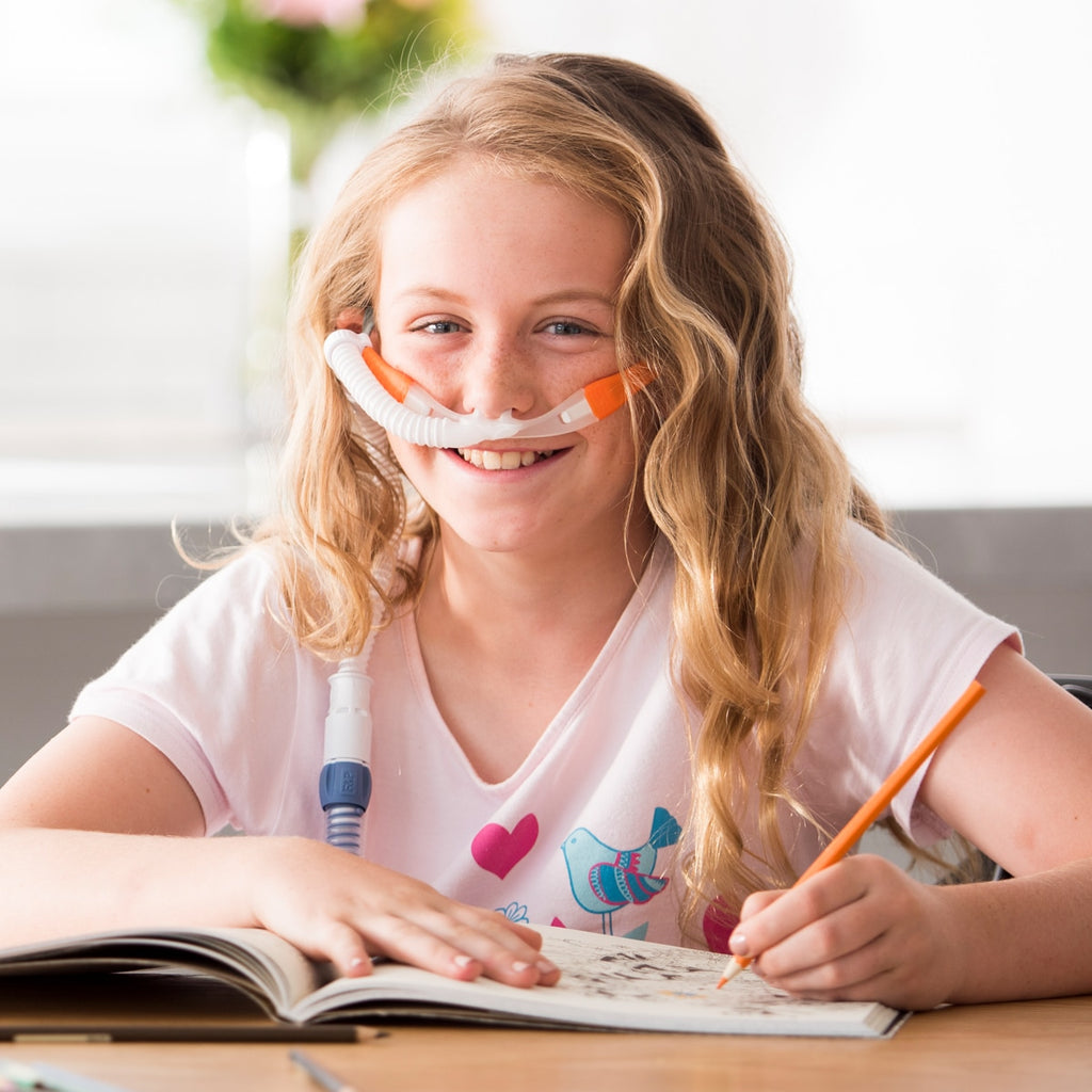 Girl wearing myAIRVO orange cannula while writing in book 