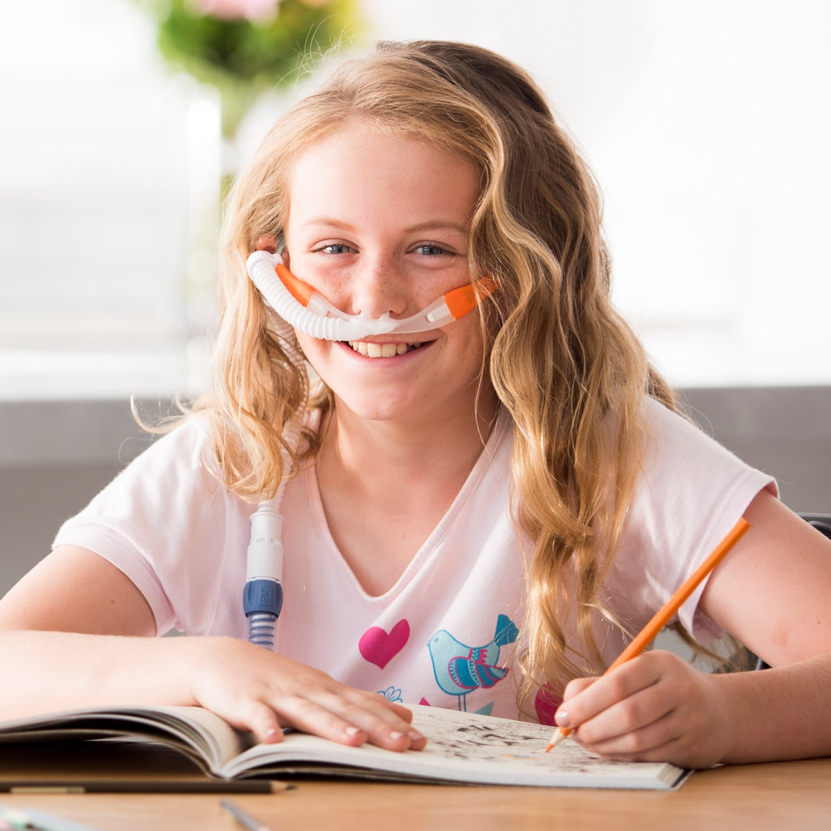 Girl wearing myAIRVO orange cannula while writing in book 