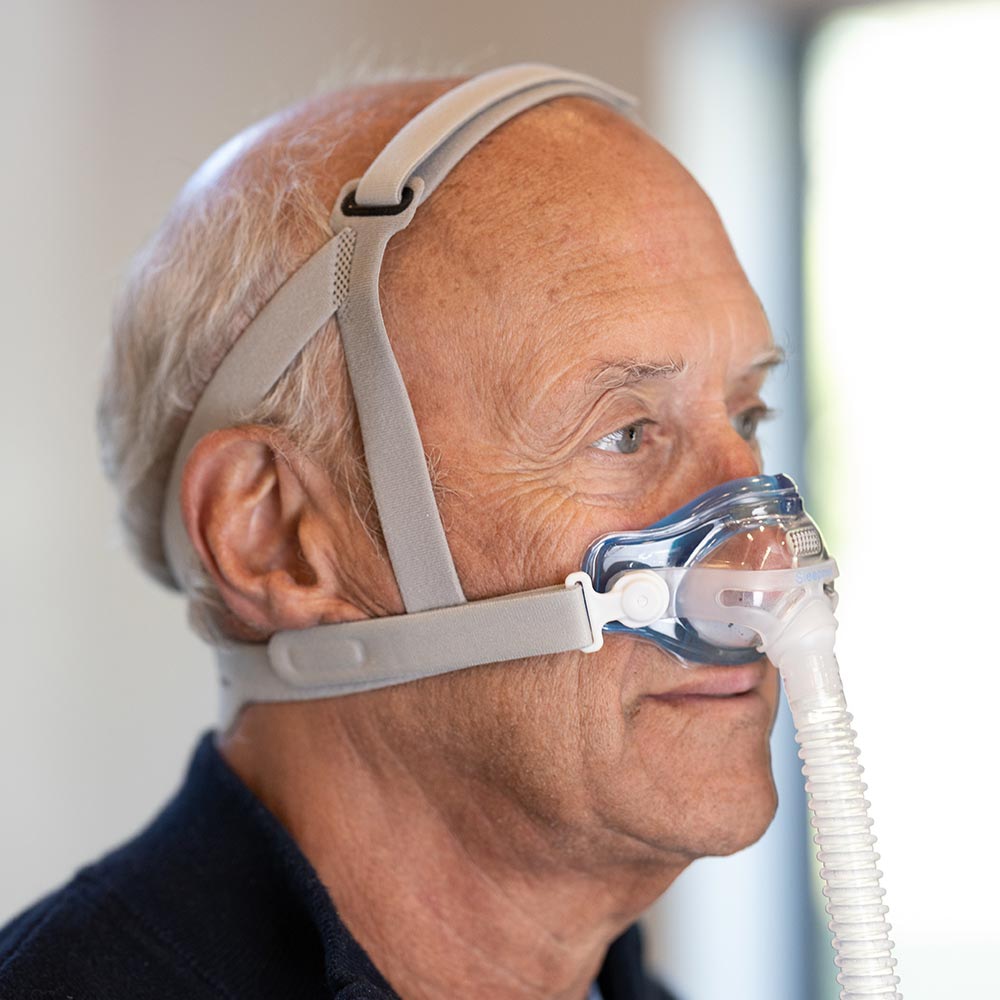 Man wearing a CPAP mask with a clear faceplate and hose.