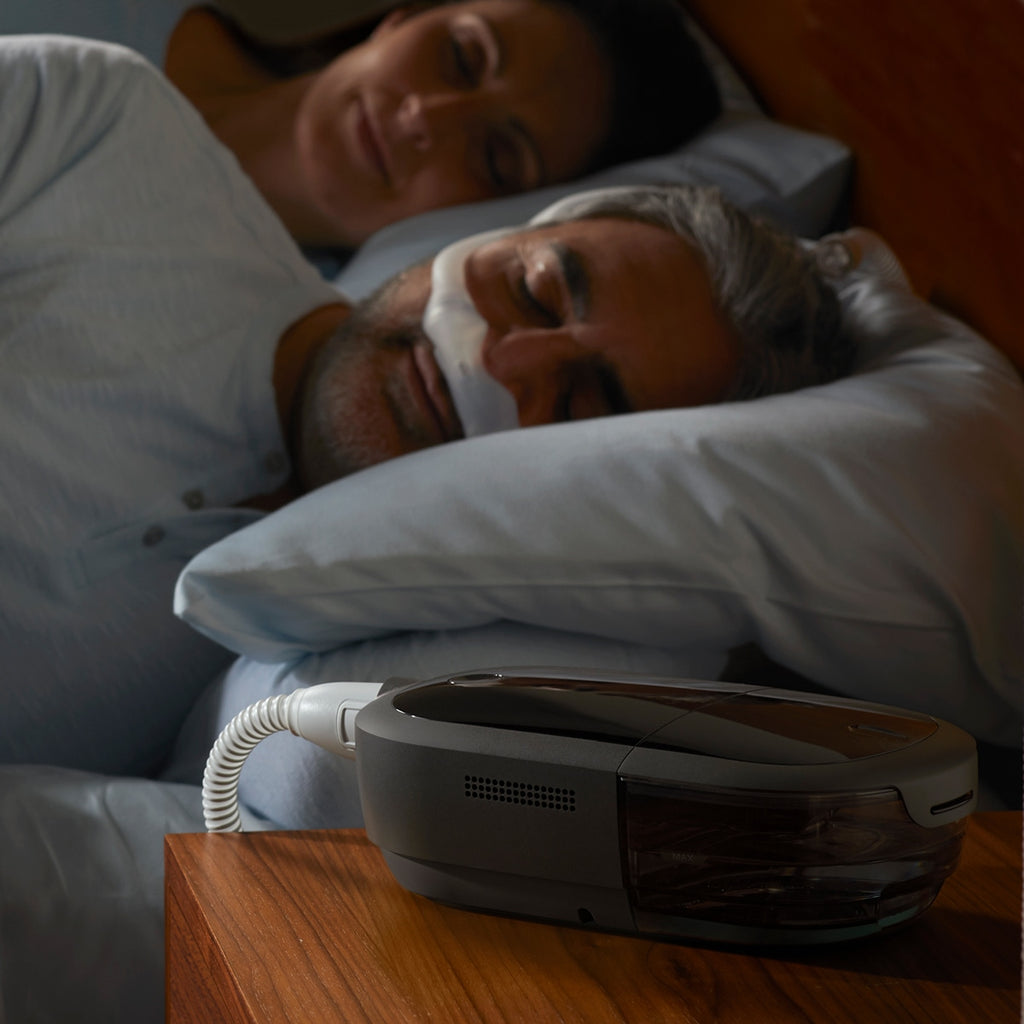 Two people sleeping with a CPAP machine on a nightstand.