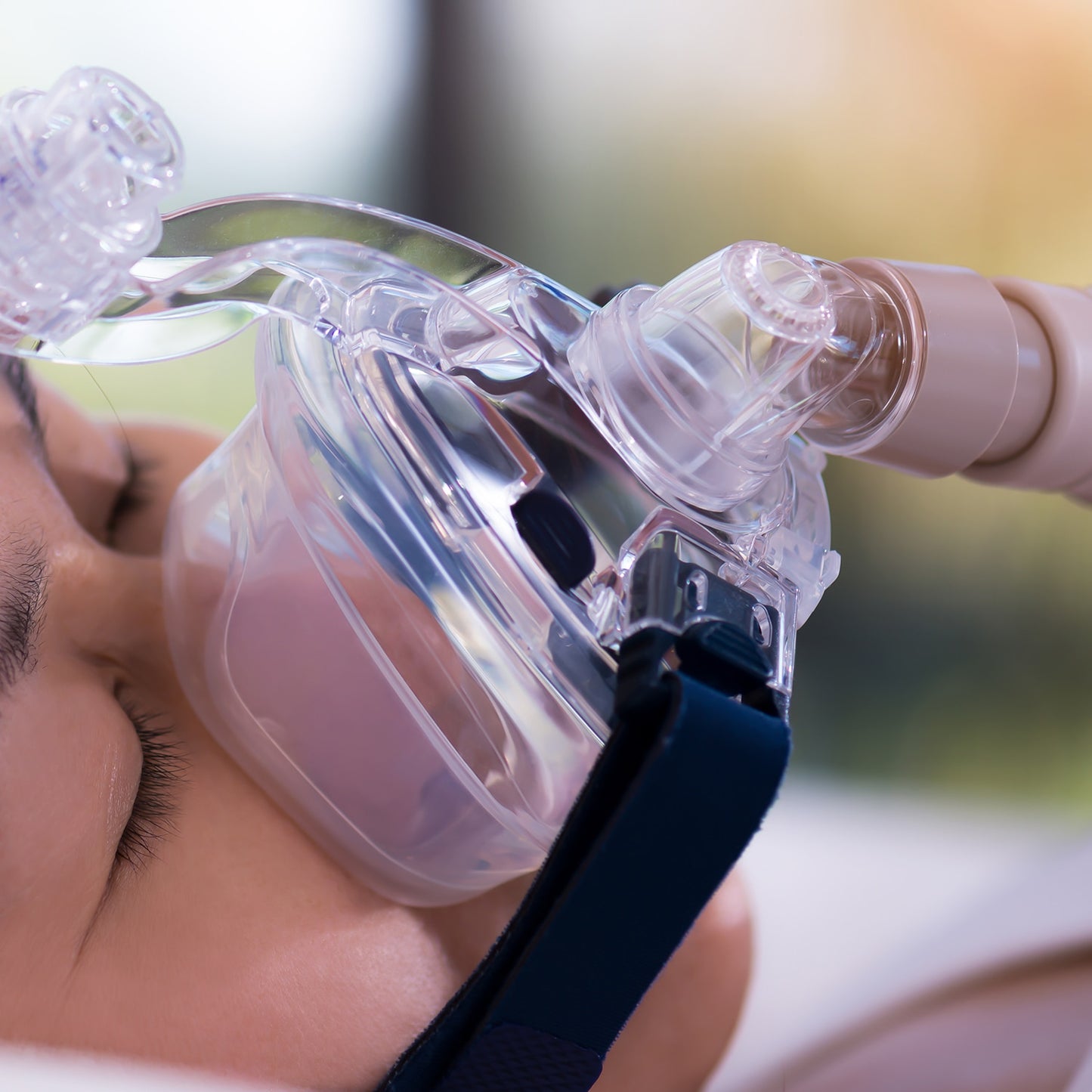 Close-up of a person using a clear CPAP mask with a blurred background