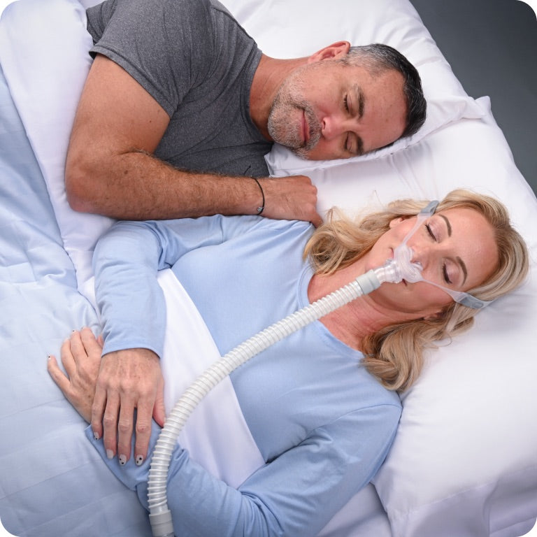 Man and woman lying in bed with a woman using a CPAP machine.