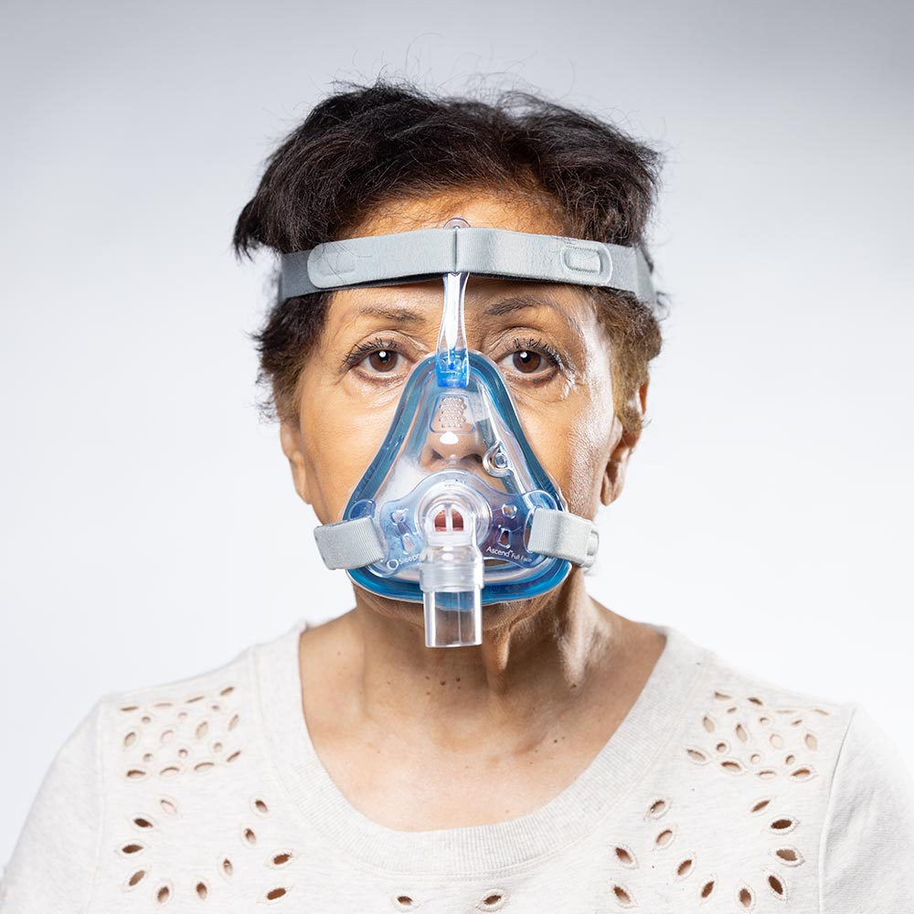 Person wearing a blue and clear CPAP mask on a white background