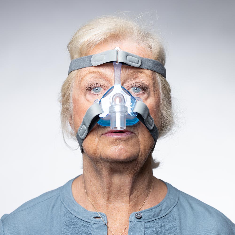 Woman wearing a CPAP mask against a plain background