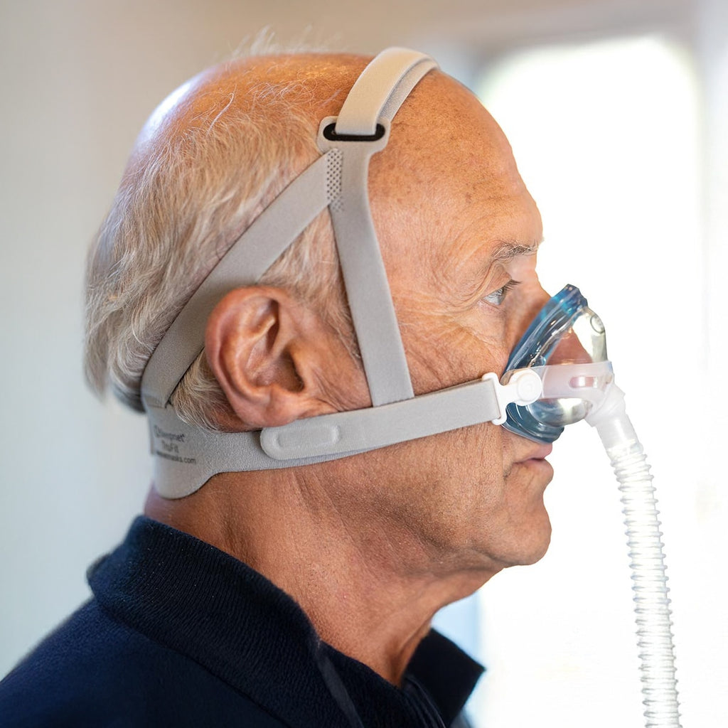 Man wearing an iQ2 CPAP mask with a clear hose on a neutral background