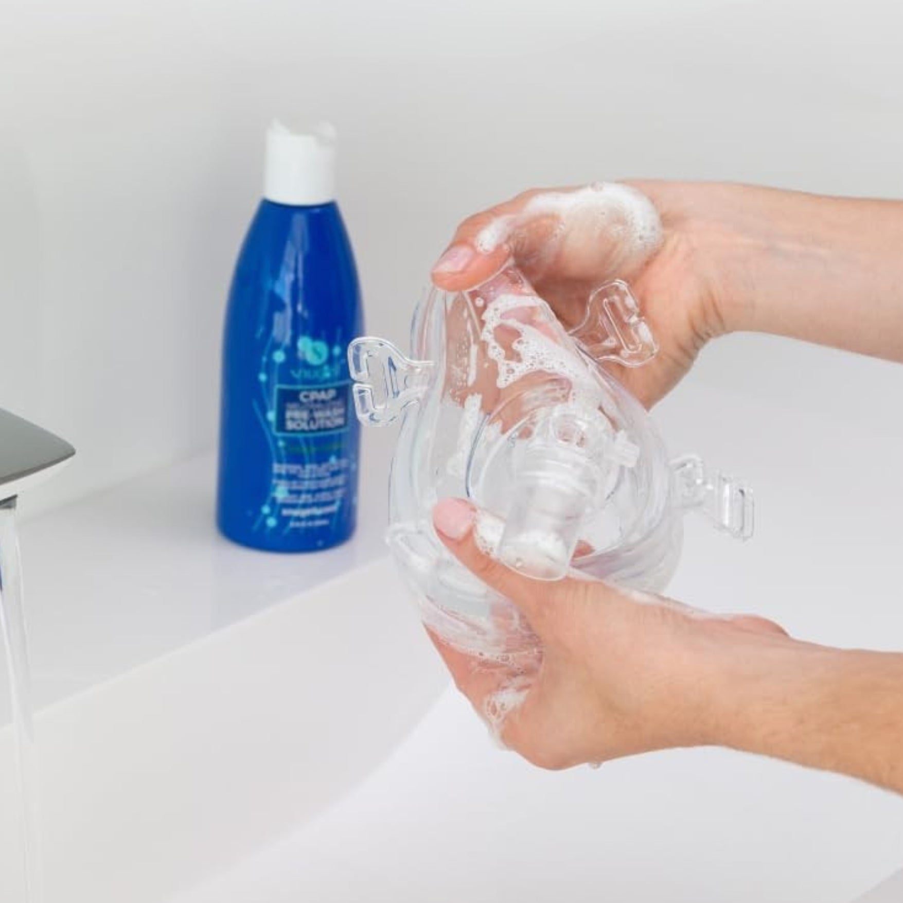hands washing a CPAP Mask with a bottle of Snuggle pre wash solution in the back 