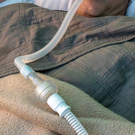Person wearing a CPAP mask with a hose on a beige blanket