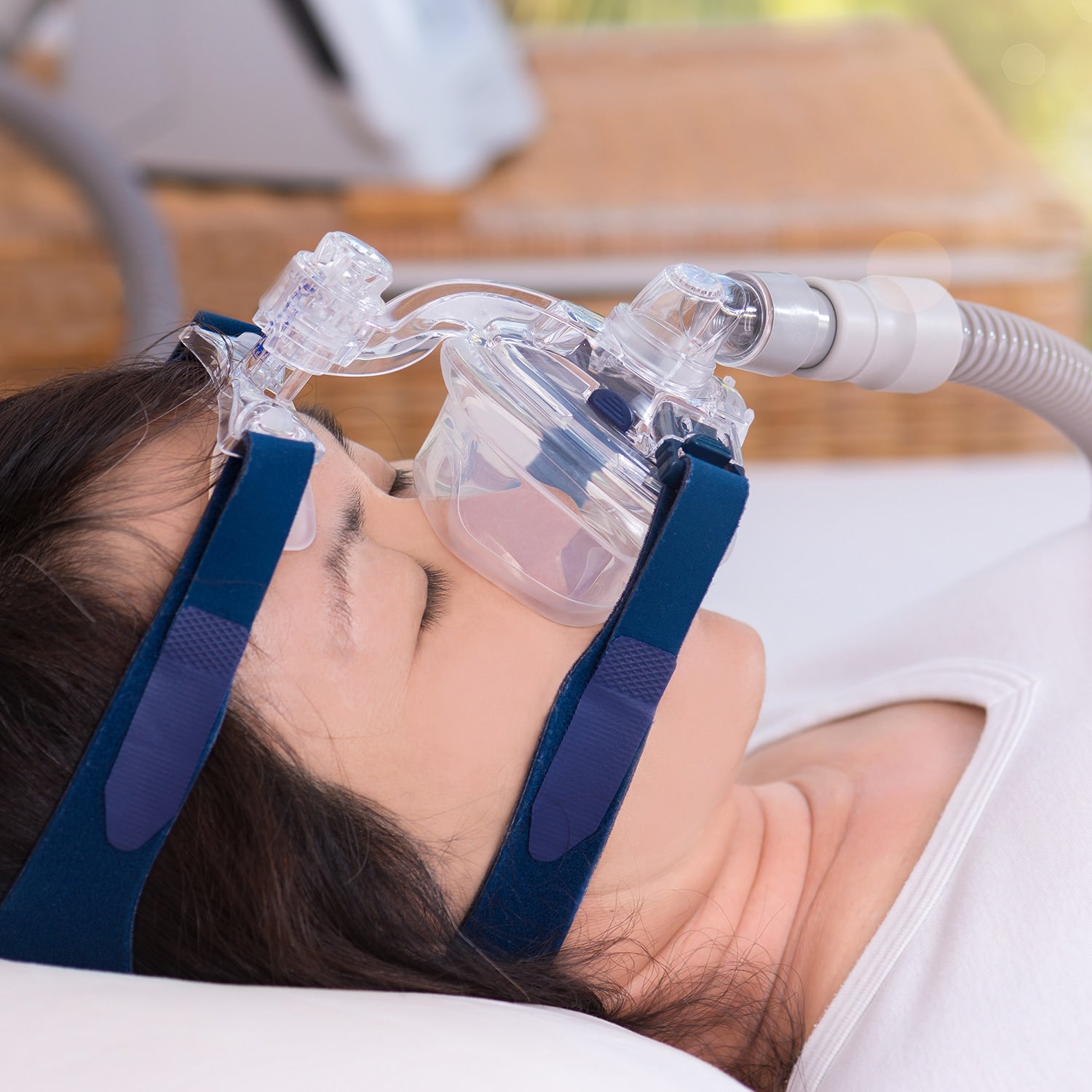 Person wearing a blue CPAP mask with a hose, lying down