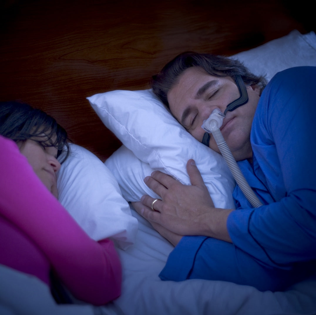 Person using a CPAP machine with another person in bed