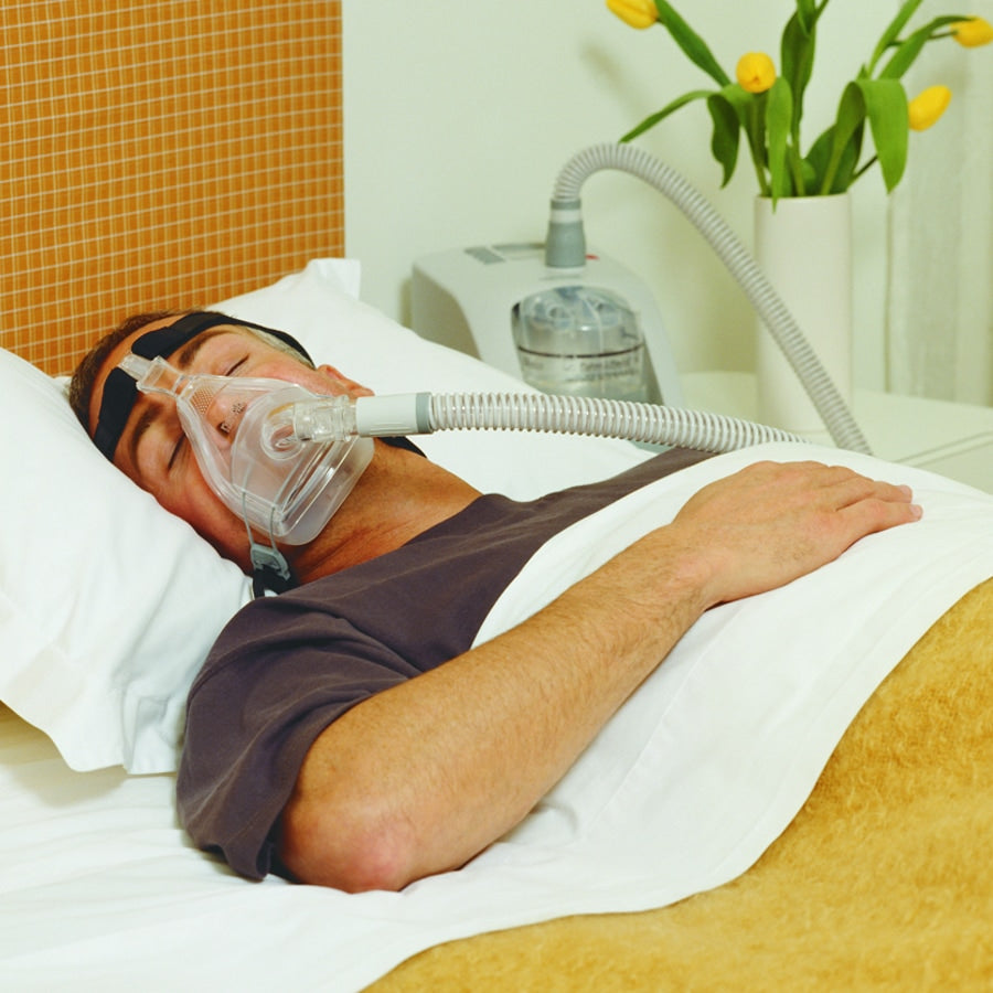 Person using a CPAP machine and FlexiFit 431 CPAP Mask  in bed with a yellow wall and plant in the background