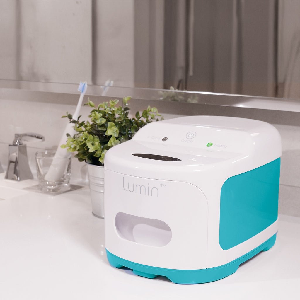 Turquoise and white Lumin device on a bathroom counter with a plant and toothbrush in the background.