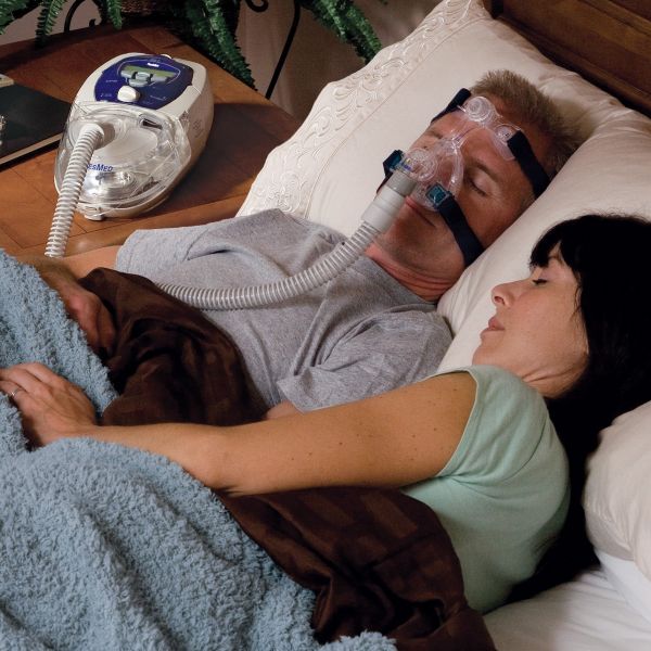 Man Sleeping in bed with a Mirago Mico CPAP Mask and CPAP Machine on night stand 