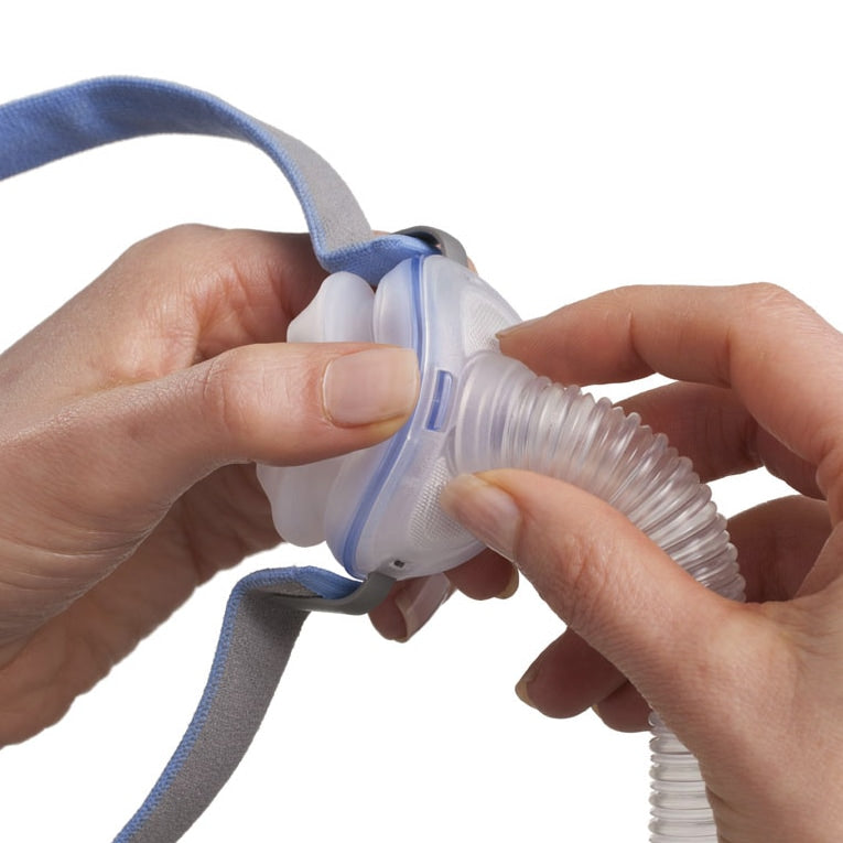 Person holding a white and blue cpap mask with a coiled tube on a white background