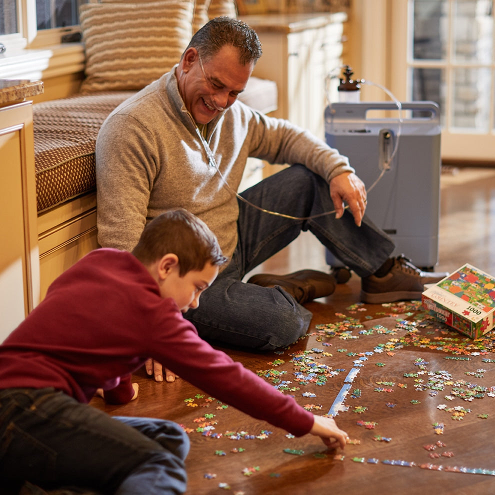 Man sitting on floor doing a puzzle while wearing Everflo Q Concentrator 