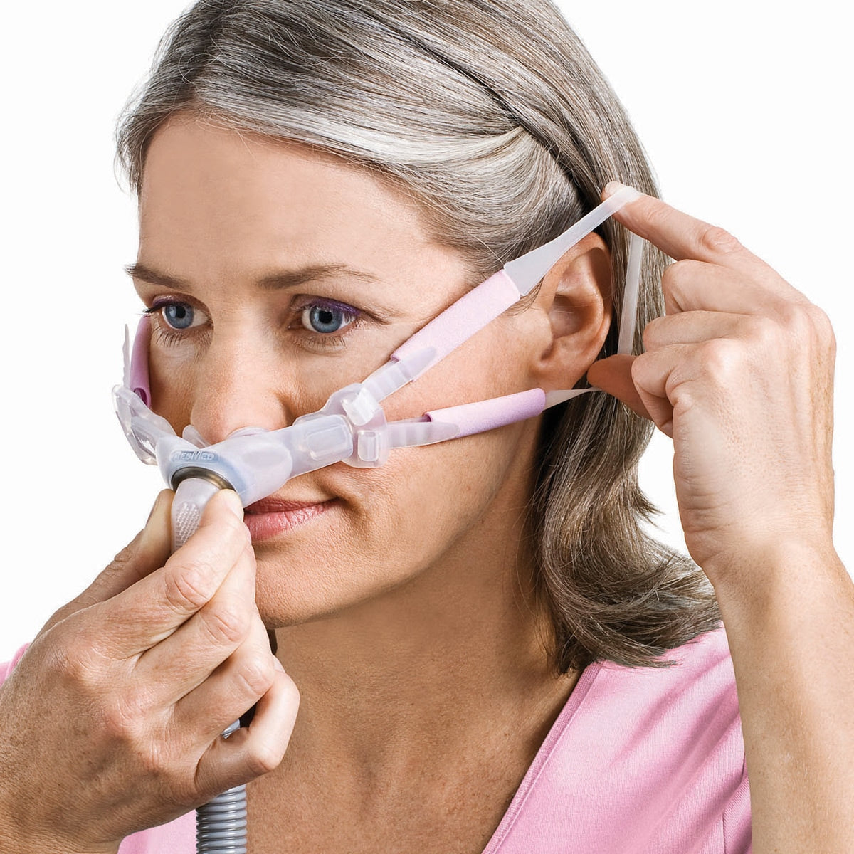 Woman adjusting a pink and gray CPAP mask on a white background